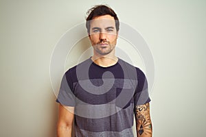 Young handsome man with tattoo wearing casual t-shirt over isolated white background with serious expression on face