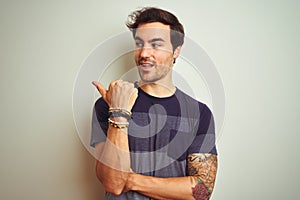 Young handsome man with tattoo wearing casual t-shirt over isolated white background smiling with happy face looking and pointing