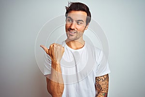 Young handsome man with tattoo wearing casual t-shirt over isolated white background smiling with happy face looking and pointing