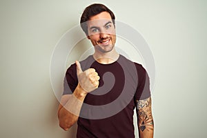 Young handsome man with tattoo wearing purple casual t-shirt over isolated white background doing happy thumbs up gesture with