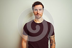 Young handsome man with tattoo wearing purple casual t-shirt over isolated white background Relaxed with serious expression on