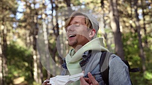 Young handsome man traveler taking off protective medical mask from face, smiling hiking in the forest. Safe travel tourism. Happy