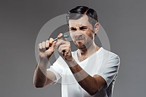 Young handsome man trying to break shaver over grey background.