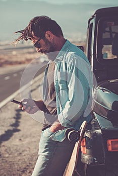 Young handsome man use phone cellular outside the black car vehicle with long road in background - travel people adventure concept