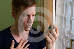 Young handsome man using asthma inhaler at home