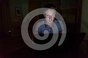 Young handsome man using laptop in the dark living room