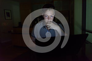 Young handsome man using laptop in the dark living room