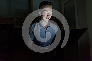 Young handsome man using laptop in the dark living room