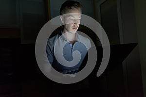 Young handsome man using laptop in the dark living room