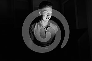 Young handsome man using laptop in the dark living room