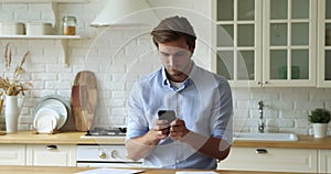 Young handsome man using mobile applications in kitchen.