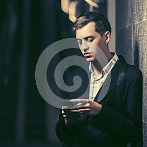 Young handsome man using smart phone standing at the wall
