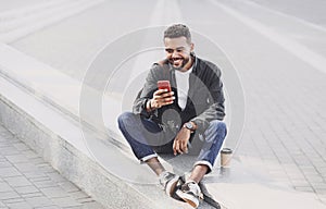 Young handsome man using smartphone in a city. Smiling student men texting on his mobile phone. Coffee break