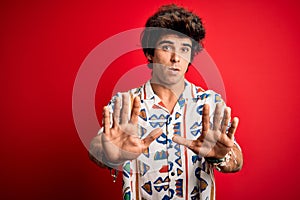 Young handsome man on vacation wearing summer shirt over isolated red background Moving away hands palms showing refusal and