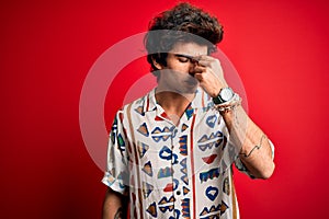 Young handsome man on vacation wearing summer shirt over isolated red background tired rubbing nose and eyes feeling fatigue and