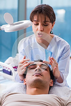 The young handsome man visiting female doctor cosmetologist