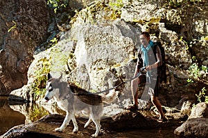 Young handsome man walking with huskies dog in canyon near water.