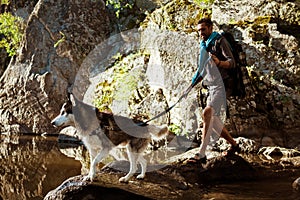 Young handsome man walking with huskies dog in canyon near water.