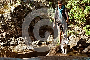 Young handsome man walking with huskies dog in canyon near water.