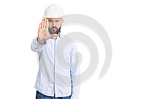 Young handsome man wearing architect hardhat doing stop sing with palm of the hand