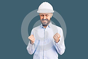 Young handsome man wearing architect hardhat excited for success with arms raised and eyes closed celebrating victory smiling