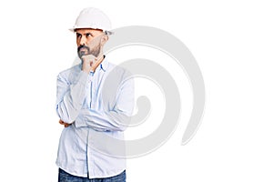 Young handsome man wearing architect hardhat with hand on chin thinking about question, pensive expression
