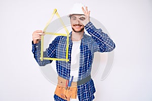 Young handsome man wearing architect hardhat holding build project smiling happy doing ok sign with hand on eye looking through