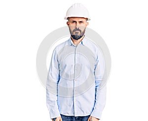 Young handsome man wearing architect hardhat relaxed with serious expression on face