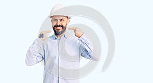 Young handsome man wearing architect hardhat smiling cheerful showing and pointing with fingers teeth and mouth