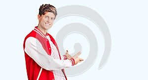 Young handsome man wearing baseball uniform inviting to enter smiling natural with open hand