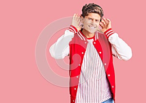 Young handsome man wearing baseball uniform trying to hear both hands on ear gesture, curious for gossip