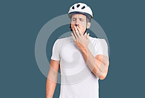 Young handsome man wearing bike helmet bored yawning tired covering mouth with hand