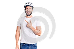 Young handsome man wearing bike helmet cheerful with a smile of face pointing with hand and finger up to the side with happy and