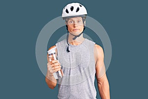 Young handsome man wearing bike helmet holding bottle of water thinking attitude and sober expression looking self confident