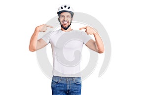 Young handsome man wearing bike helmet looking confident with smile on face, pointing oneself with fingers proud and happy