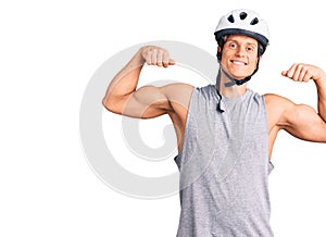 Young handsome man wearing bike helmet showing arms muscles smiling proud