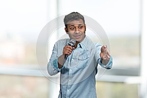 Young handsome man wearing blue shirt speaking to microphone pointing with index finger to the side.