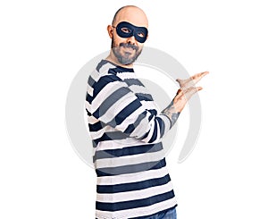 Young handsome man wearing burglar mask inviting to enter smiling natural with open hand