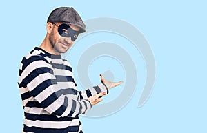 Young handsome man wearing burglar mask inviting to enter smiling natural with open hand