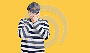 Young handsome man wearing burglar mask shocked covering mouth with hands for mistake