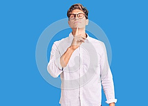 Young handsome man wearing business clothes and glasses thinking concentrated about doubt with finger on chin and looking up