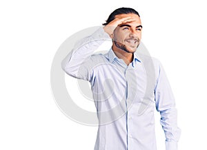 Young handsome man wearing business clothes very happy and smiling looking far away with hand over head