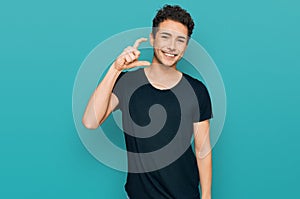 Young handsome man wearing casual black t shirt smiling and confident gesturing with hand doing small size sign with fingers