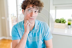 Young handsome man wearing casual blue t-shirt at home with hand on chin thinking about question, pensive expression