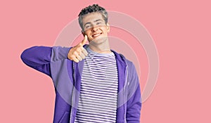 Young handsome man wearing casual purple sweatshirt doing happy thumbs up gesture with hand