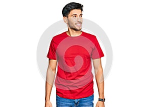 Young handsome man wearing casual red tshirt looking away to side with smile on face, natural expression