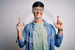 Young handsome man wearing casual shirt and glasses over isolated white background gesturing finger crossed smiling with hope and