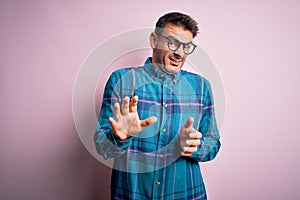 Young handsome man wearing casual shirt and glasses standing over isolated pink background disgusted expression, displeased and