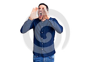 Young handsome man wearing casual shirt shouting angry out loud with hands over mouth