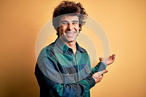 Young handsome man wearing casual shirt standing over isolated yellow background Inviting to enter smiling natural with open hand